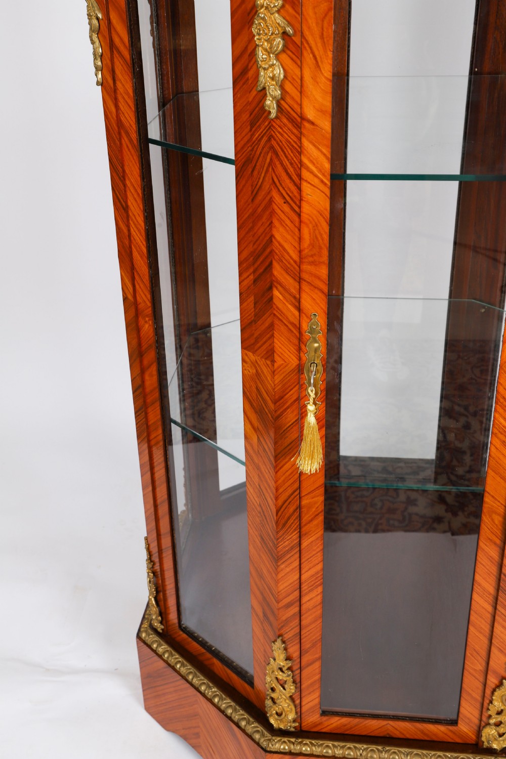 An octagonal kingwood display cabinet featuring chevron parquetry veneers, gilt bronze mounts, and glazed panels housing internal glass shelves. View IX