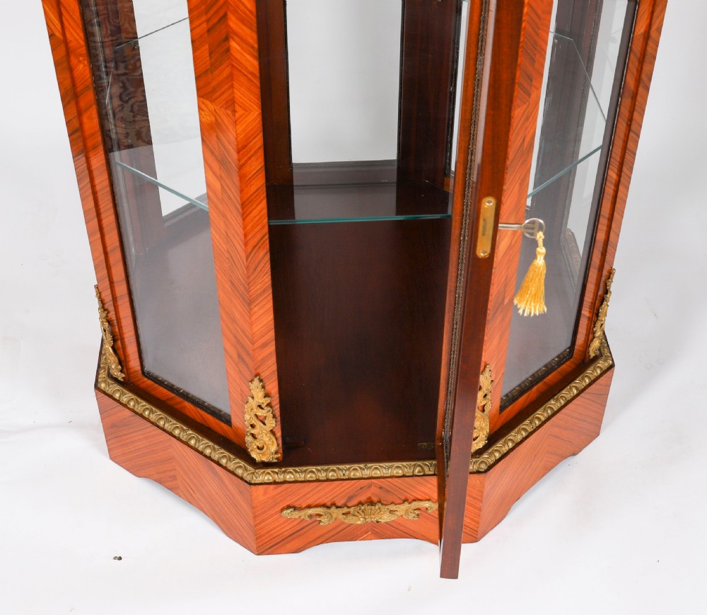 An octagonal kingwood display cabinet featuring chevron parquetry veneers, gilt bronze mounts, and glazed panels housing internal glass shelves. View X