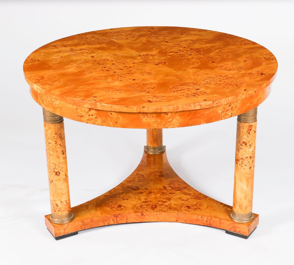 A circular 20th-century Biedermeier revival coffee table made from burr elm with three column legs set on a triform plinth base.