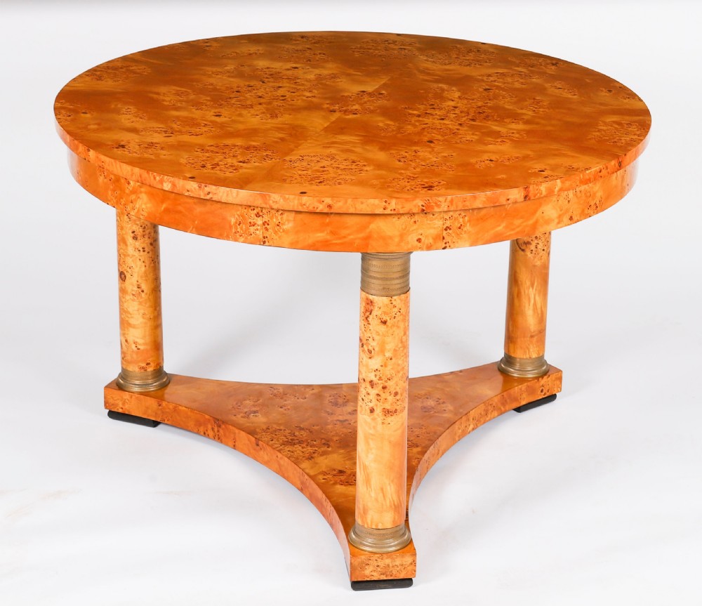 A circular 20th-century Biedermeier revival coffee table made from burr elm with three column legs set on a triform plinth base. View II