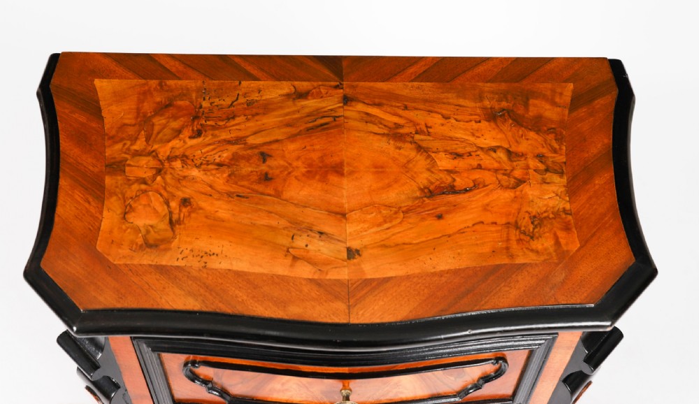 A pair of 18th-century Italian burr walnut serpentine bedside chests featuring ebonised mouldings, three drawers, and scroll feet. View V