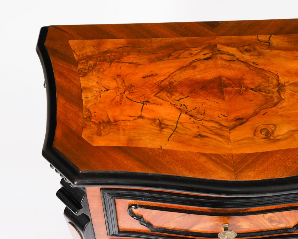 A pair of 18th-century Italian burr walnut serpentine bedside chests featuring ebonised mouldings, three drawers, and scroll feet. View VI