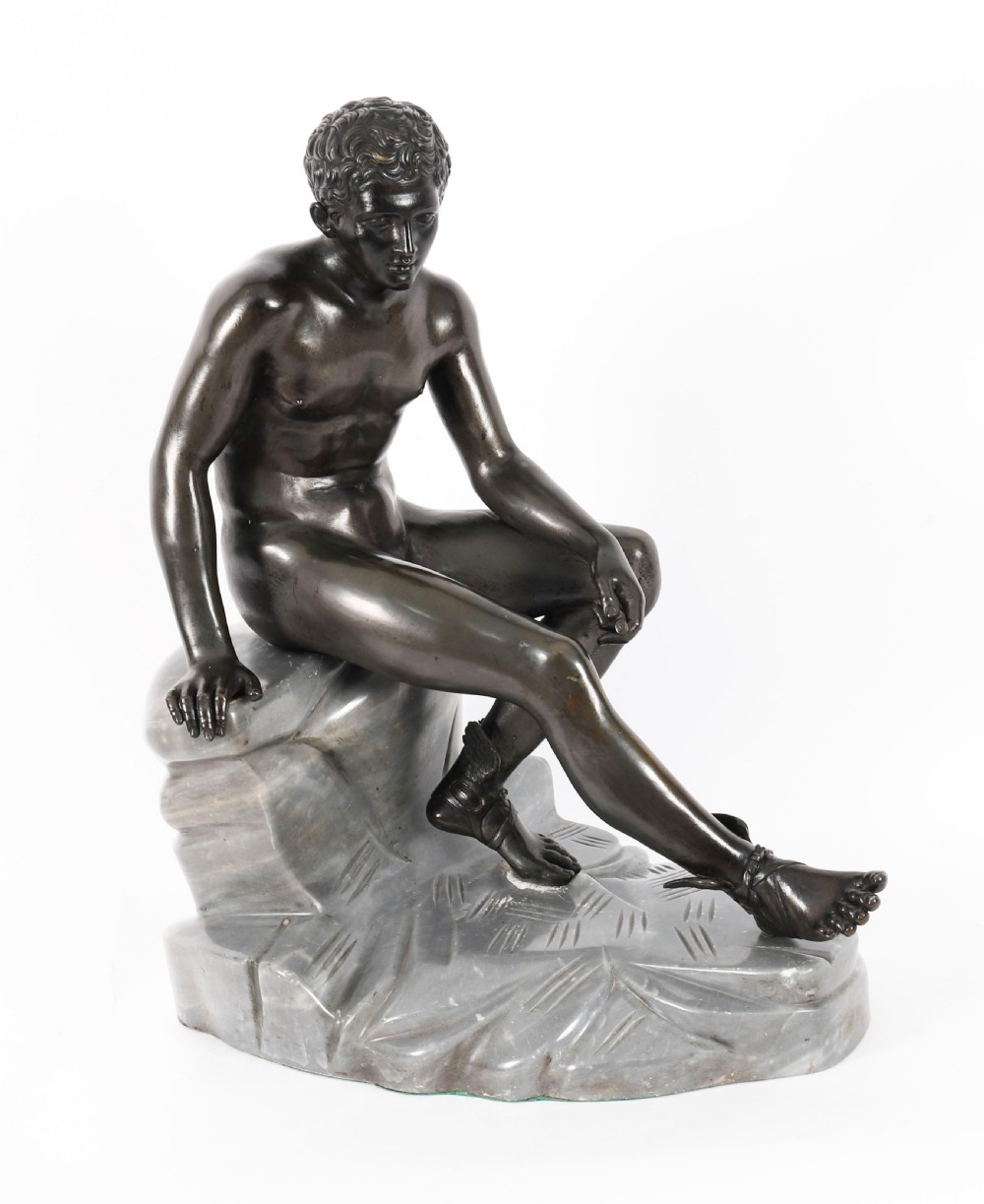 A dark patinated bronze sculpture depicting a nude seated Hermes resting on a carved grey marble base.