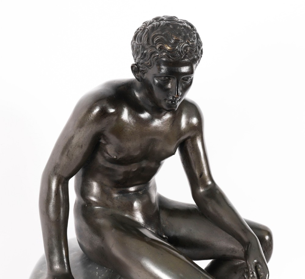A dark patinated bronze sculpture depicting a nude seated Hermes resting on a carved grey marble base. View IV
