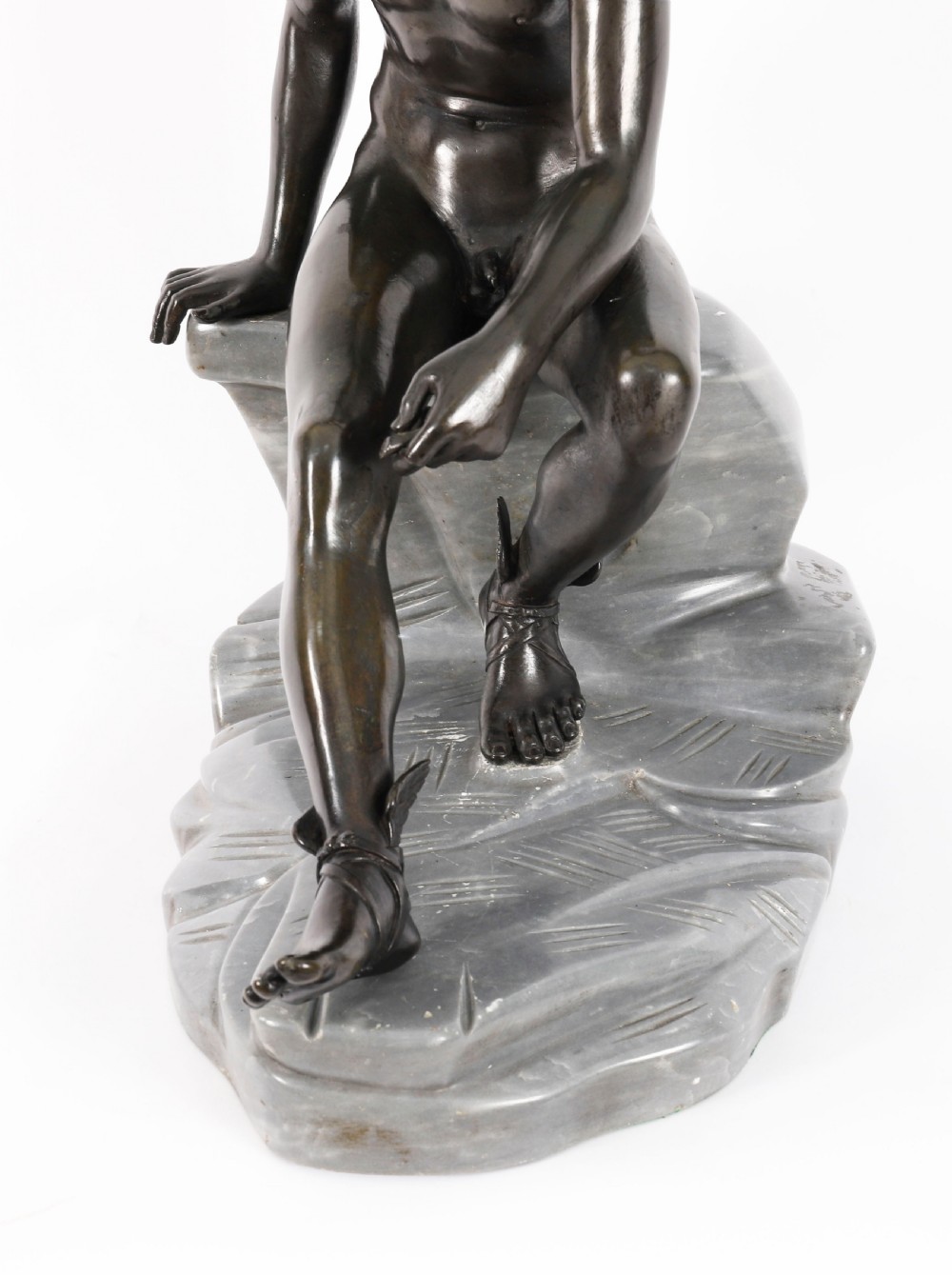 A dark patinated bronze sculpture depicting a nude seated Hermes resting on a carved grey marble base. View X