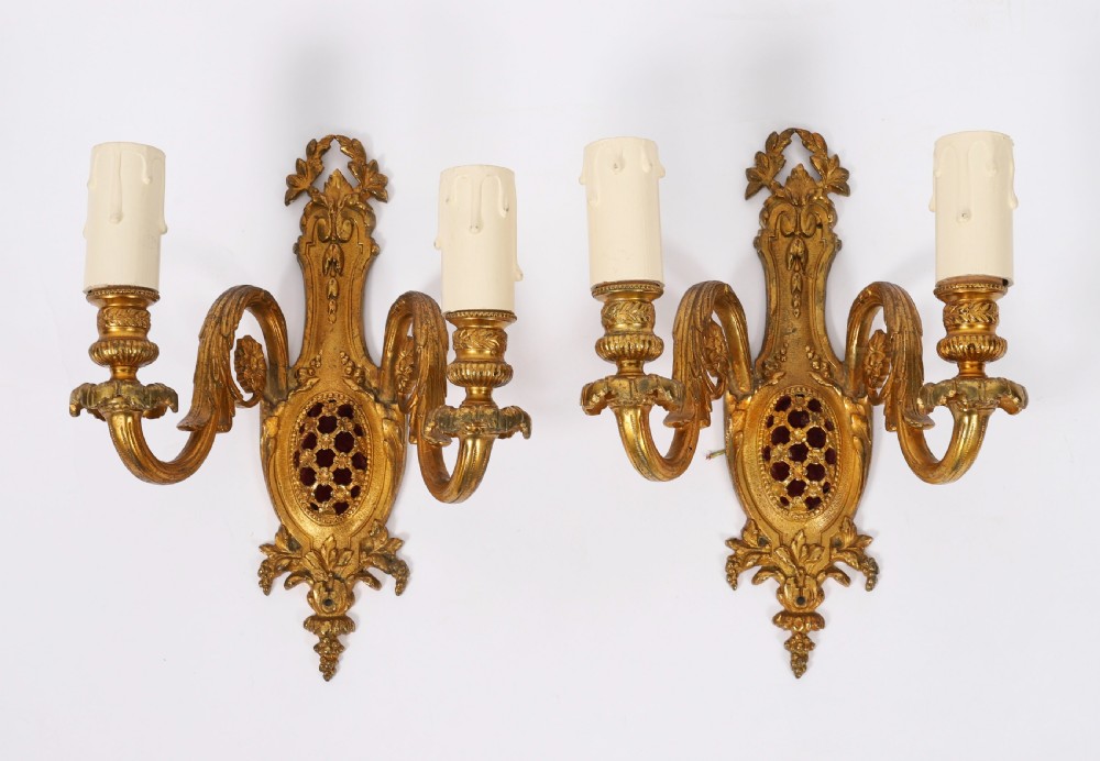 A pair of 19th-century French gilt bronze twin-light wall appliques featuring floral cresting, acanthus leaf arms, and faux candle sleeves.