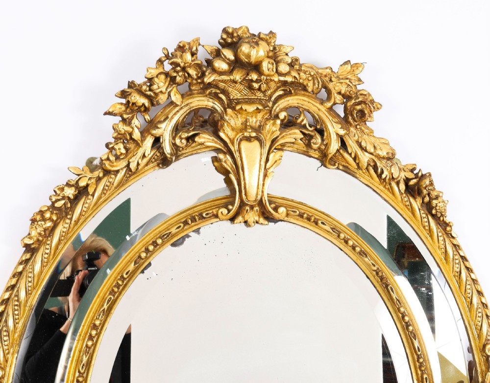 An ornate nineteenth-century oval giltwood cushion mirror featuring carved floral cresting, acanthus leaf accents, and surround mirror paneling. View II