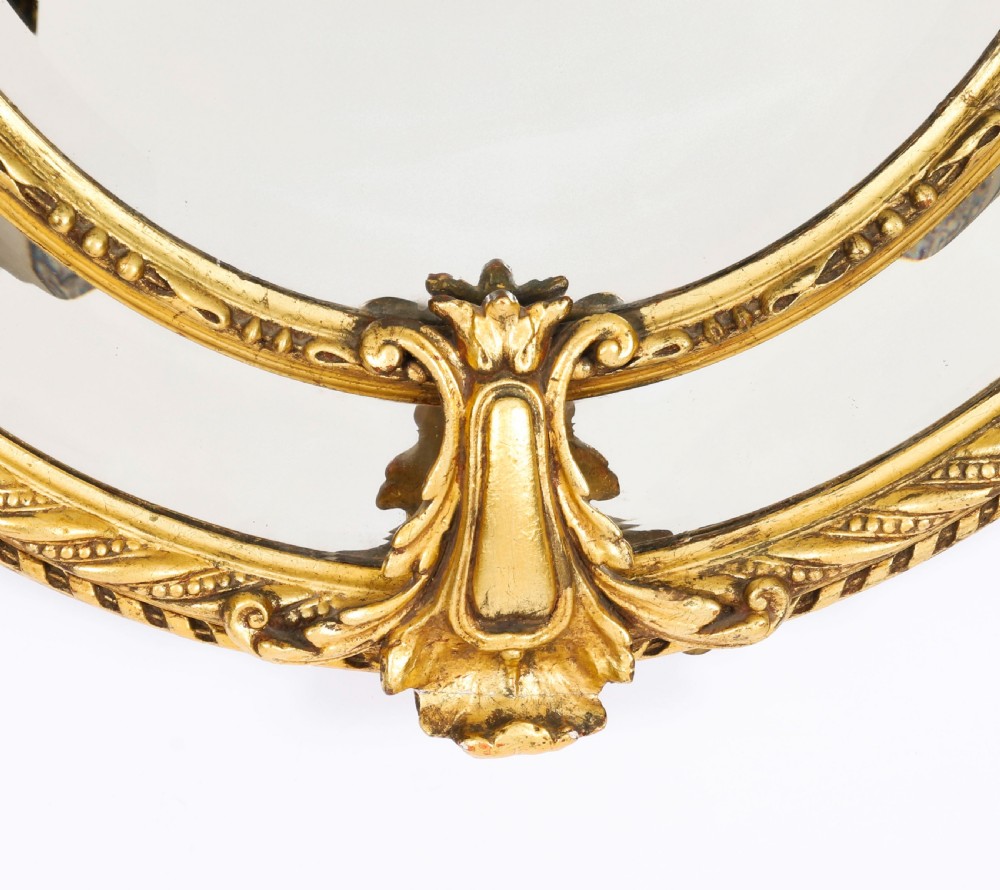An ornate nineteenth-century oval giltwood cushion mirror featuring carved floral cresting, acanthus leaf accents, and surround mirror paneling. View III