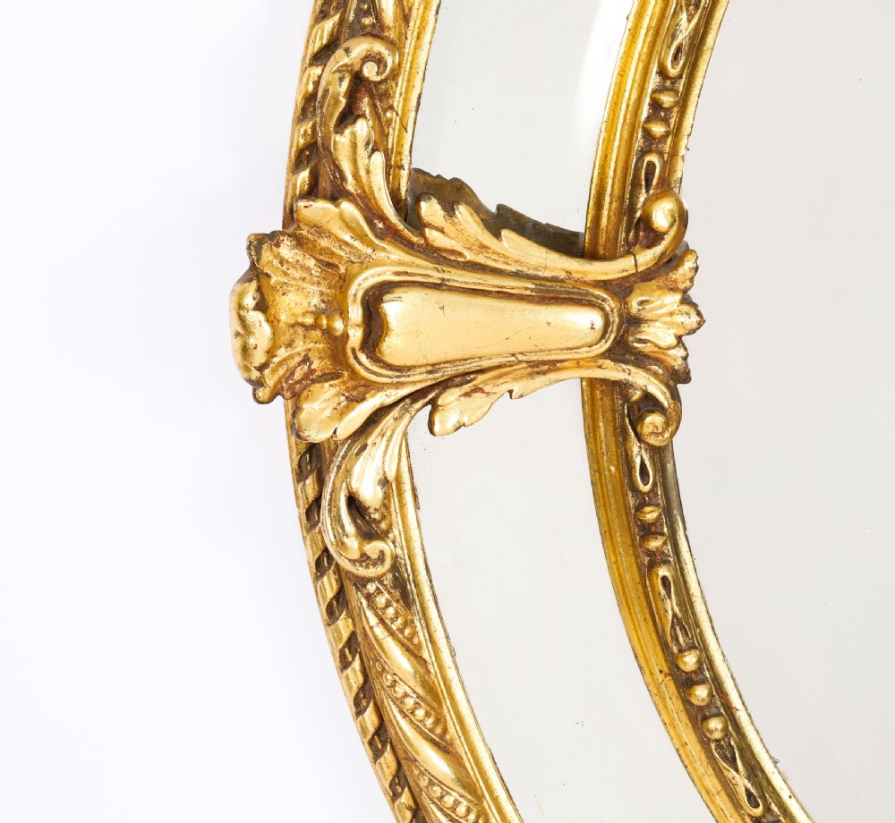 An ornate nineteenth-century oval giltwood cushion mirror featuring carved floral cresting, acanthus leaf accents, and surround mirror paneling. View IV
