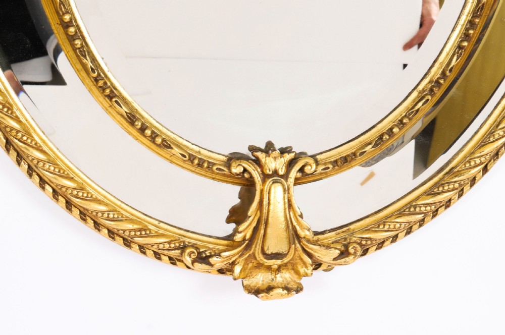 An ornate nineteenth-century oval giltwood cushion mirror featuring carved floral cresting, acanthus leaf accents, and surround mirror paneling. View VI