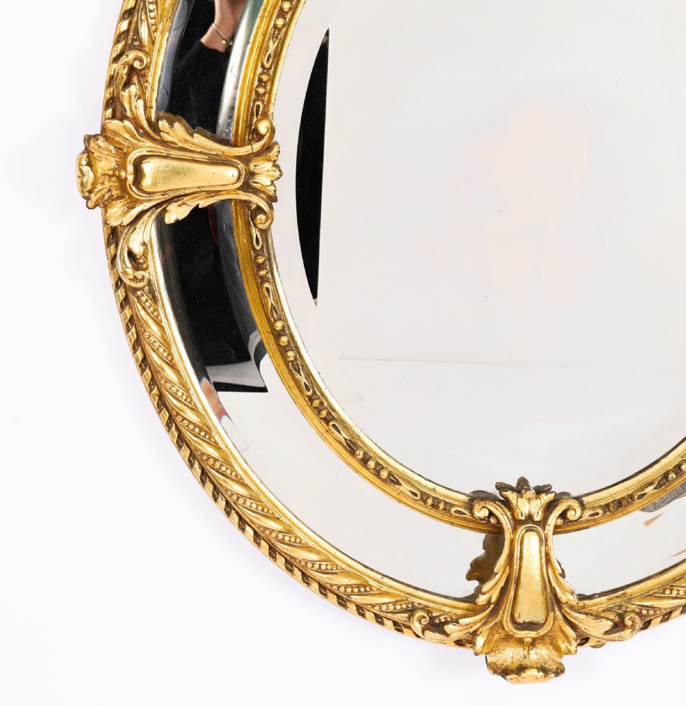 An ornate nineteenth-century oval giltwood cushion mirror featuring carved floral cresting, acanthus leaf accents, and surround mirror paneling. View VII