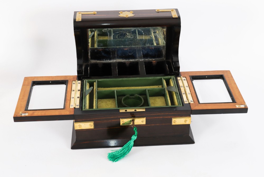A nineteenth-century coromandel wood scent bottle casket with brass mounts opening to reveal cut-glass bottles and mirrored compartments. View X