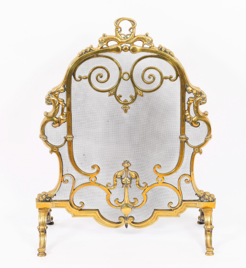 A nineteenth-century French Louis Revival brass fire screen featuring a wire mesh panel, scrollwork details, and dolphin motifs supported by four splayed feet. View II