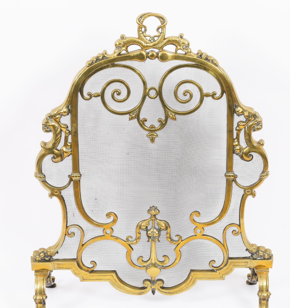 A nineteenth-century French Louis Revival brass fire screen featuring a wire mesh panel, scrollwork details, and dolphin motifs supported by four splayed feet. View III