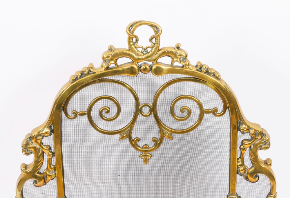 A nineteenth-century French Louis Revival brass fire screen featuring a wire mesh panel, scrollwork details, and dolphin motifs supported by four splayed feet. View IV