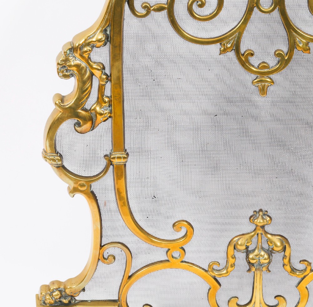 A nineteenth-century French Louis Revival brass fire screen featuring a wire mesh panel, scrollwork details, and dolphin motifs supported by four splayed feet. View V