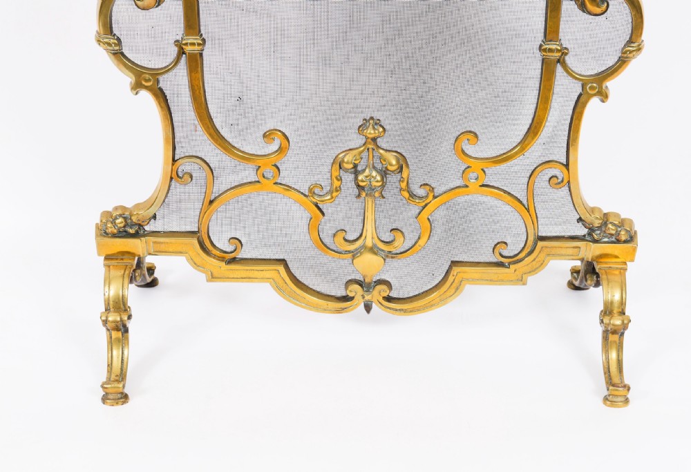 A nineteenth-century French Louis Revival brass fire screen featuring a wire mesh panel, scrollwork details, and dolphin motifs supported by four splayed feet. View VII