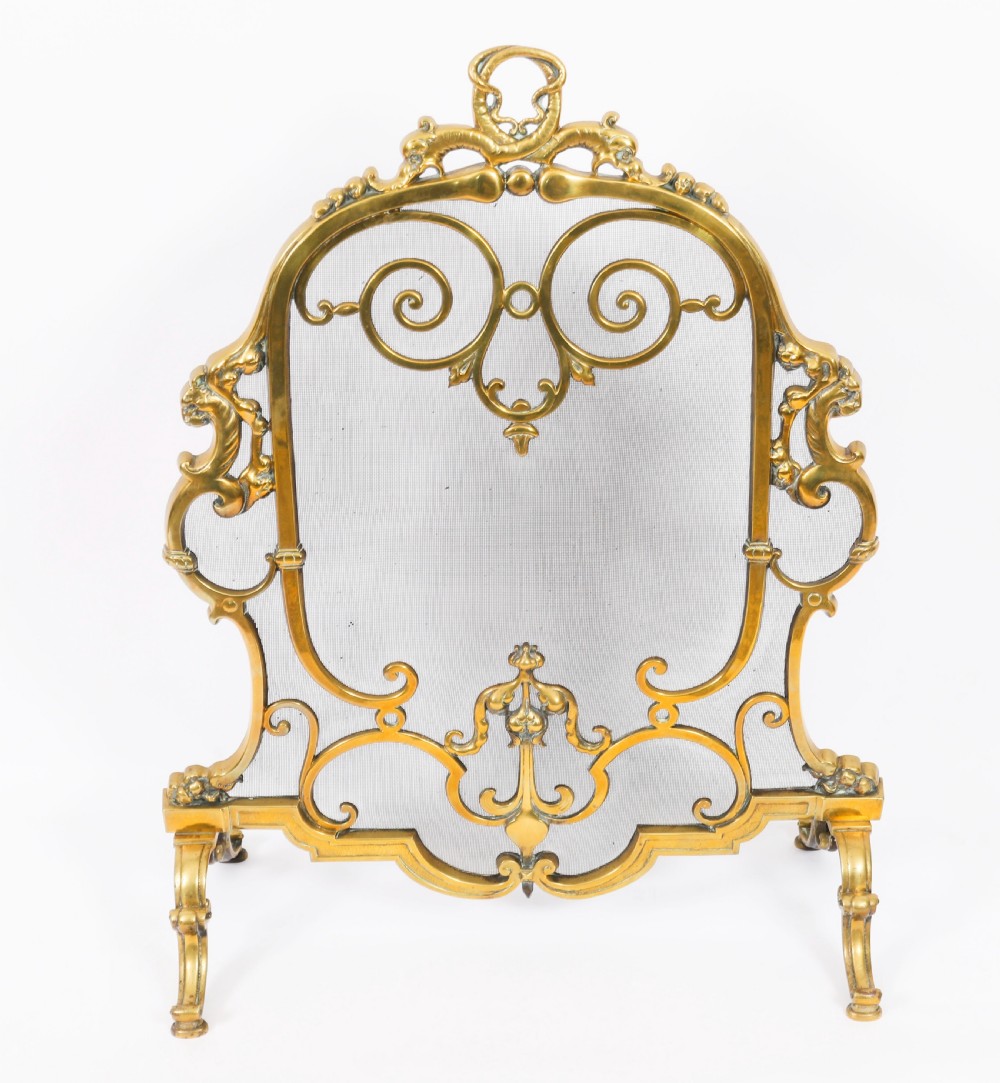A nineteenth-century French Louis Revival brass fire screen featuring a wire mesh panel, scrollwork details, and dolphin motifs supported by four splayed feet. View VIII