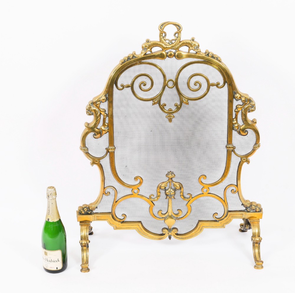 A nineteenth-century French Louis Revival brass fire screen featuring a wire mesh panel, scrollwork details, and dolphin motifs supported by four splayed feet. View IX