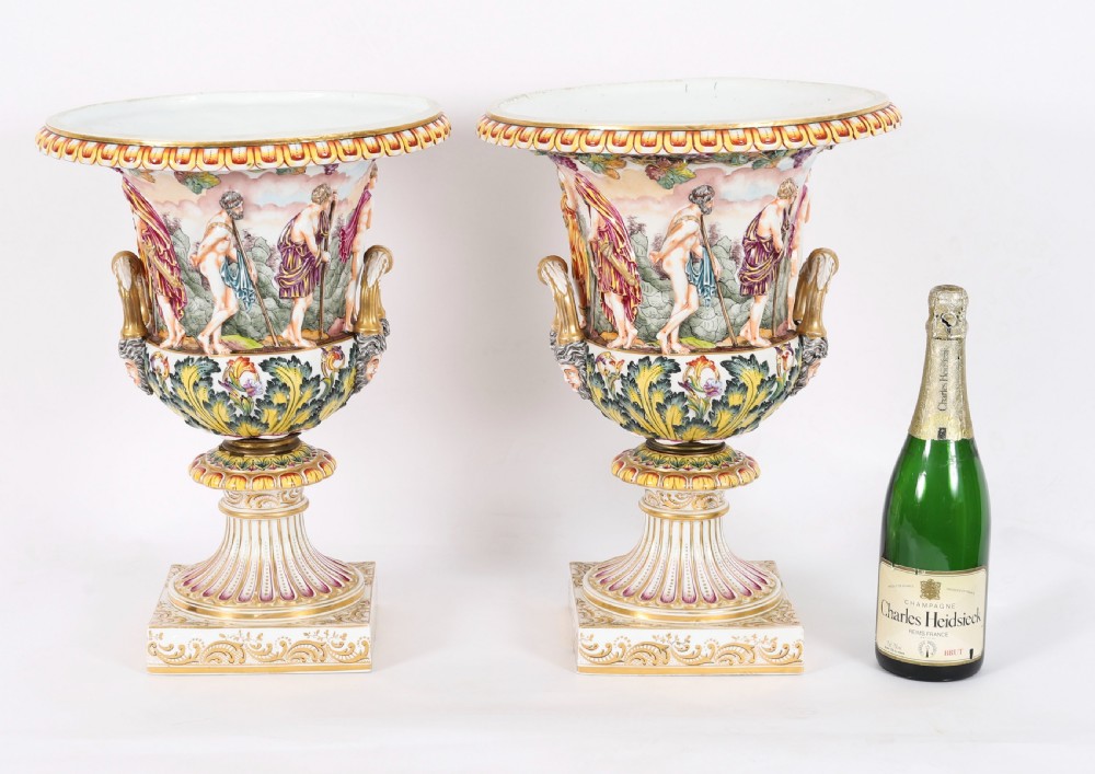 A 19th-century Capodimonte porcelain urn featuring classical figures in high relief, polychrome enamelling, gilded handles, and a square base. View XIX