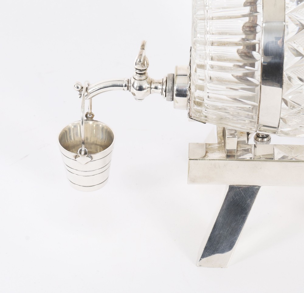 A nineteenth-century cut crystal barrel decanter with silver-plated hoops, tap, and miniature bucket accessory resting on a four-legged silver stand. View VI