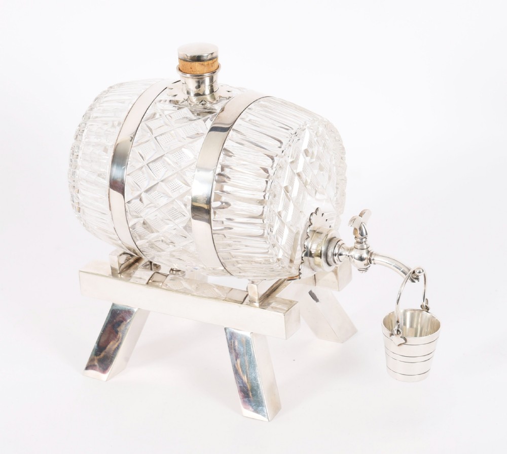 A nineteenth-century cut crystal barrel decanter with silver-plated hoops, tap, and miniature bucket accessory resting on a four-legged silver stand. View VII