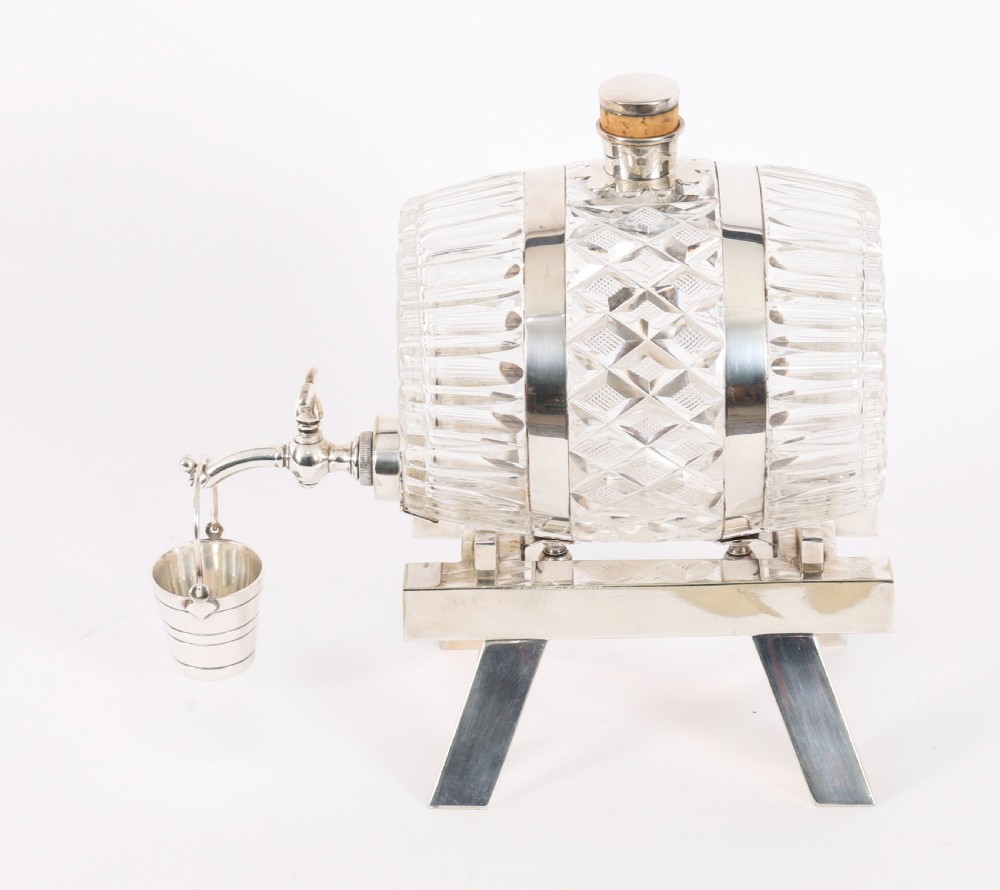 A nineteenth-century cut crystal barrel decanter with silver-plated hoops, tap, and miniature bucket accessory resting on a four-legged silver stand. View VIII