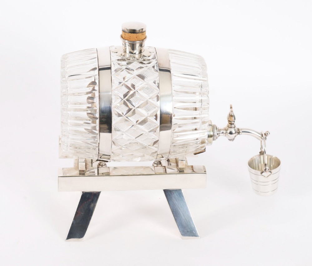 A nineteenth-century cut crystal barrel decanter with silver-plated hoops, tap, and miniature bucket accessory resting on a four-legged silver stand. View X