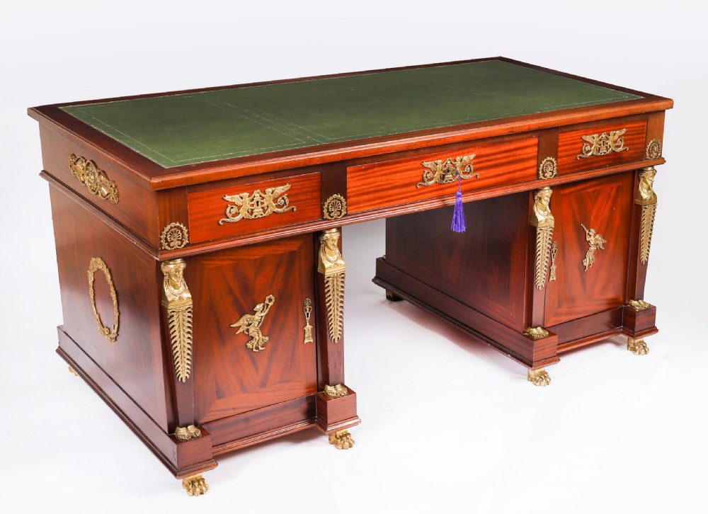A French Empire style mahogany pedestal desk featuring a green leather top insert, decorative gilt-bronze mounts, and caryatid corner supports.