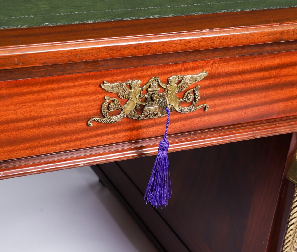 A French Empire style mahogany pedestal desk featuring a green leather top insert, decorative gilt-bronze mounts, and caryatid corner supports. View IX