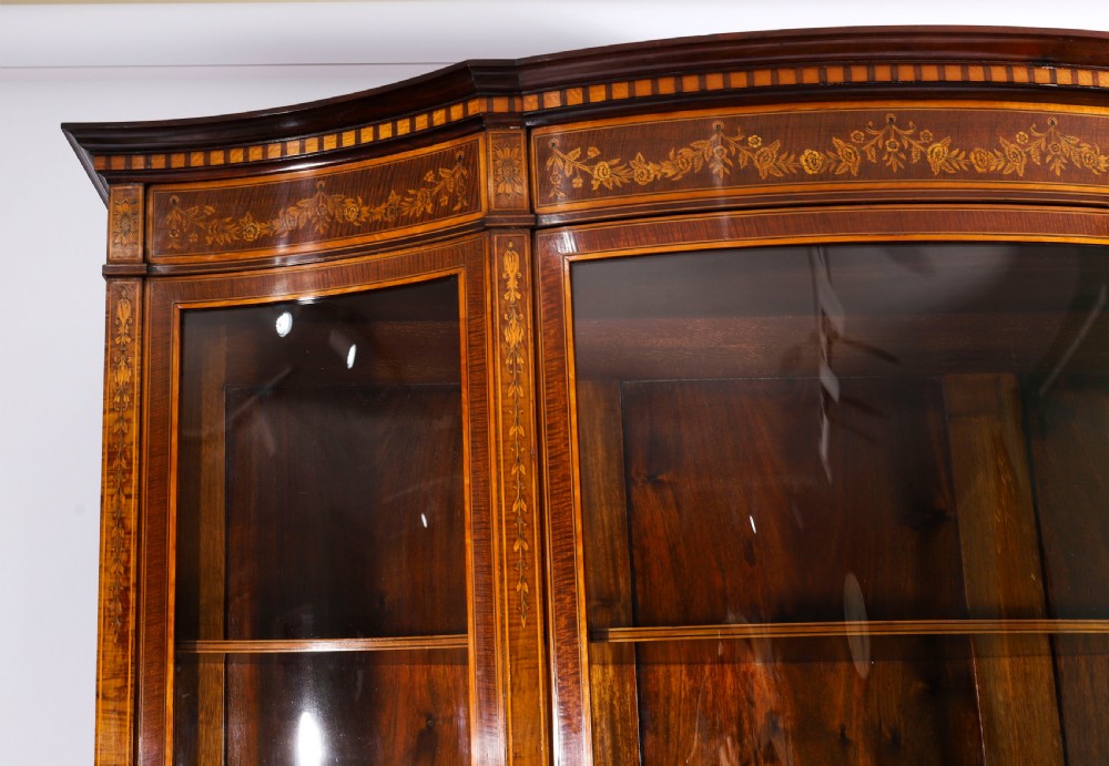 A 19th-century mahogany serpentine display cabinet featuring intricate floral marquetry inlays, three glazed upper doors, three central drawers, and tapered legs. View V