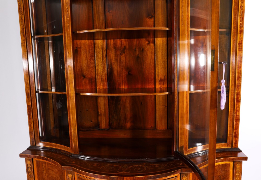 A 19th-century mahogany serpentine display cabinet featuring intricate floral marquetry inlays, three glazed upper doors, three central drawers, and tapered legs. View VI