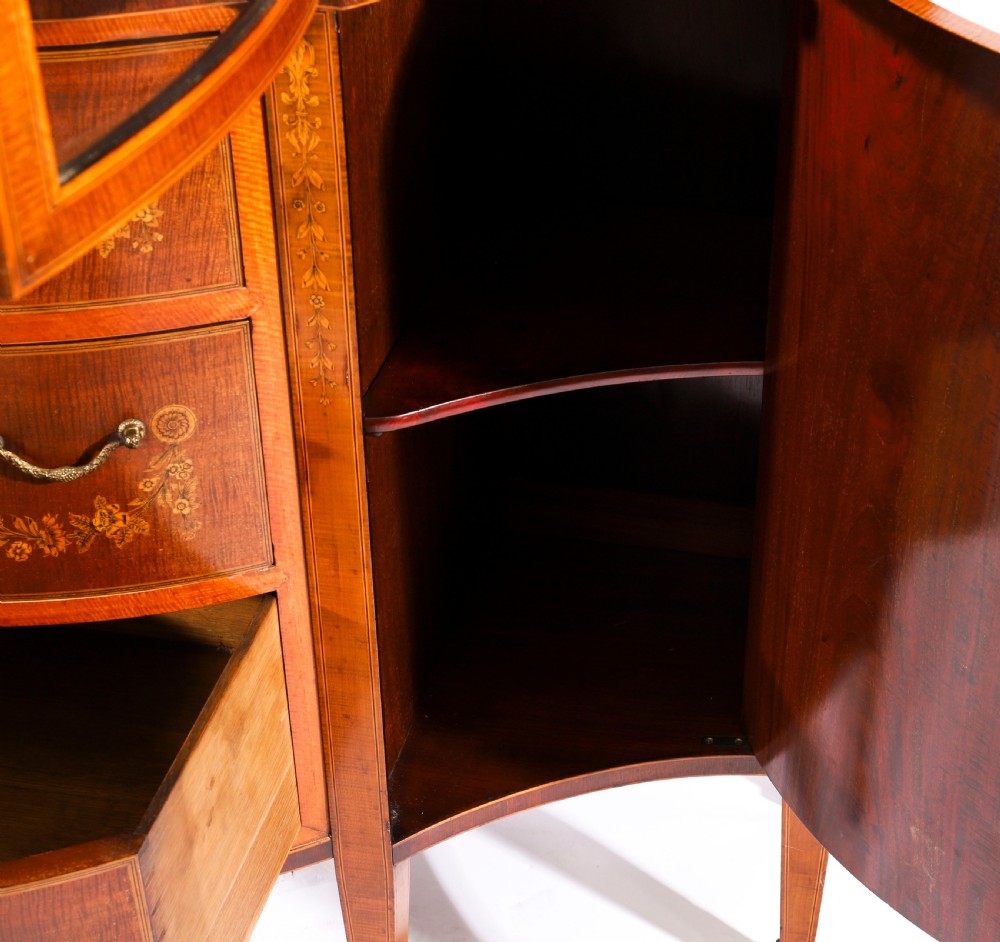 A 19th-century mahogany serpentine display cabinet featuring intricate floral marquetry inlays, three glazed upper doors, three central drawers, and tapered legs. View VII