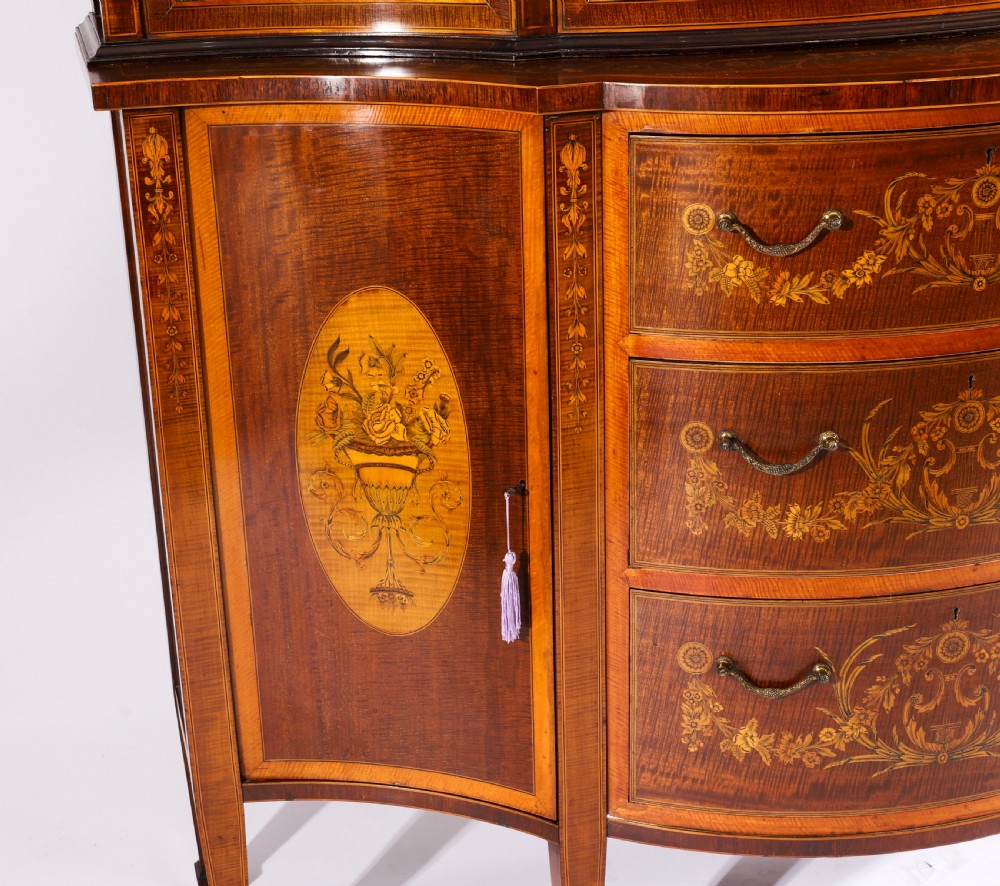 A 19th-century mahogany serpentine display cabinet featuring intricate floral marquetry inlays, three glazed upper doors, three central drawers, and tapered legs. View XI