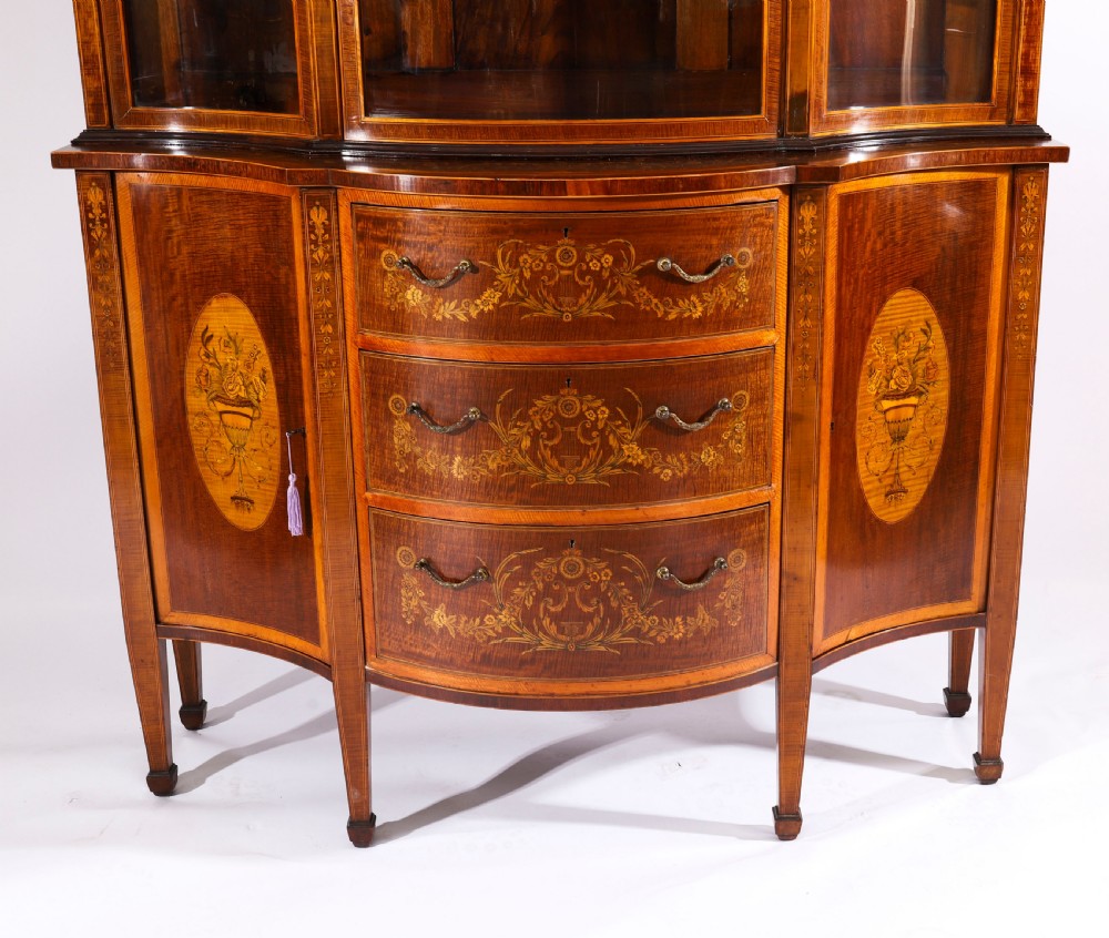 A 19th-century mahogany serpentine display cabinet featuring intricate floral marquetry inlays, three glazed upper doors, three central drawers, and tapered legs. View XII