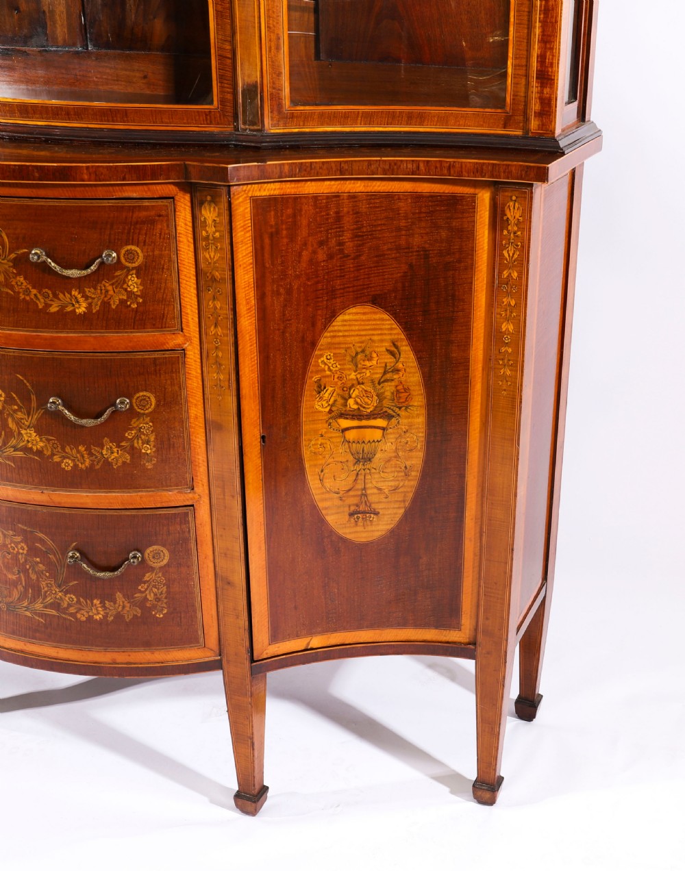 A 19th-century mahogany serpentine display cabinet featuring intricate floral marquetry inlays, three glazed upper doors, three central drawers, and tapered legs. View XIV