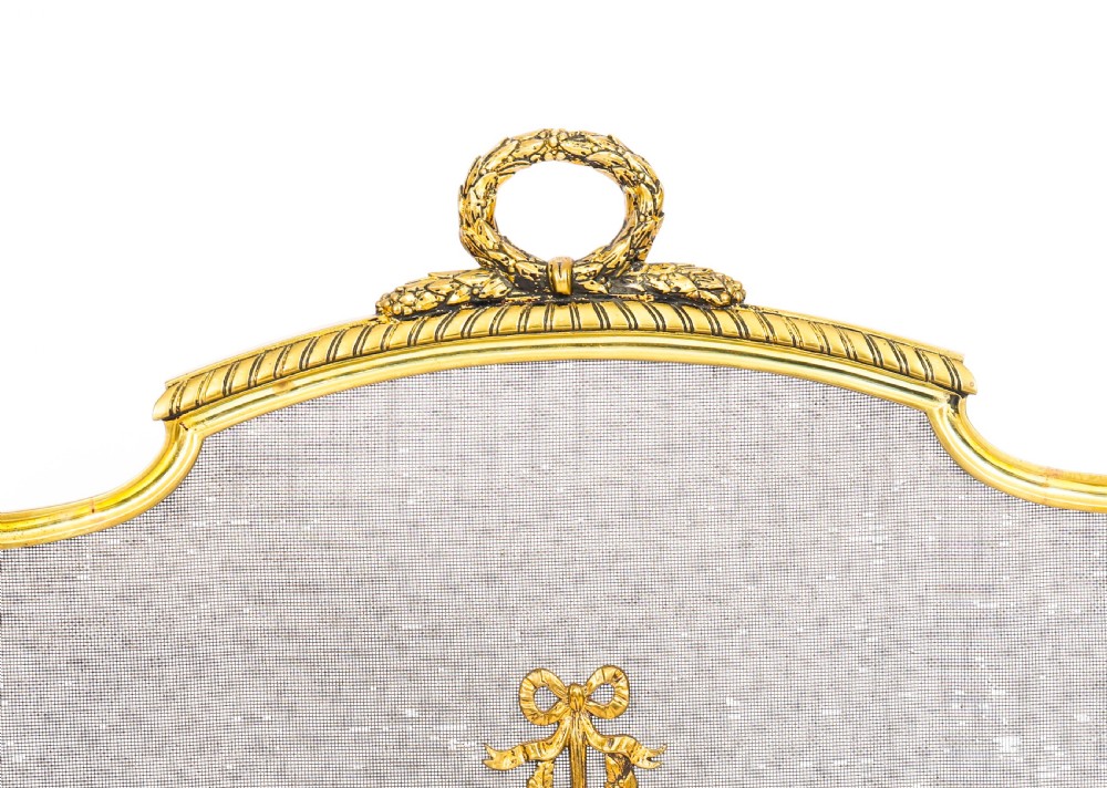 A French Empire Revival gilt bronze fire screen featuring a woven mesh panel, laurel wreath top handle, and central flaming torch motif on splayed feet. View X