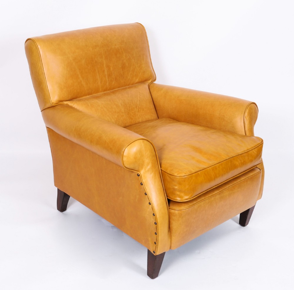 An Art Deco leather armchair upholstered in caramel tan hide with studded trim and square tapered wooden legs.