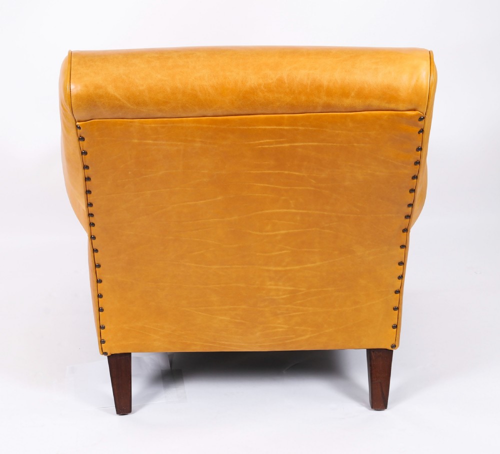 An Art Deco leather armchair upholstered in caramel tan hide with studded trim and square tapered wooden legs. View X