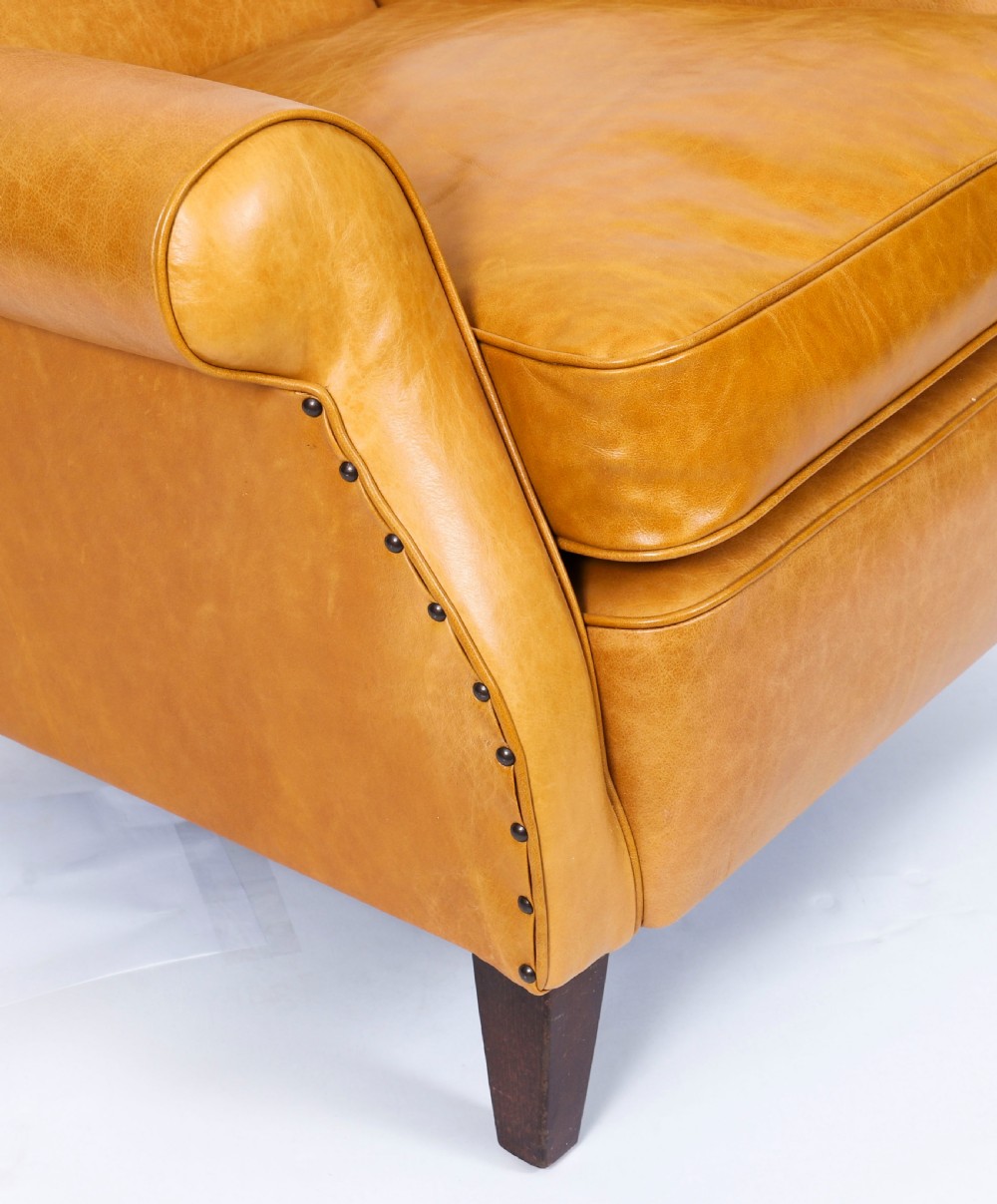 An Art Deco leather armchair upholstered in caramel tan hide with studded trim and square tapered wooden legs. View XI