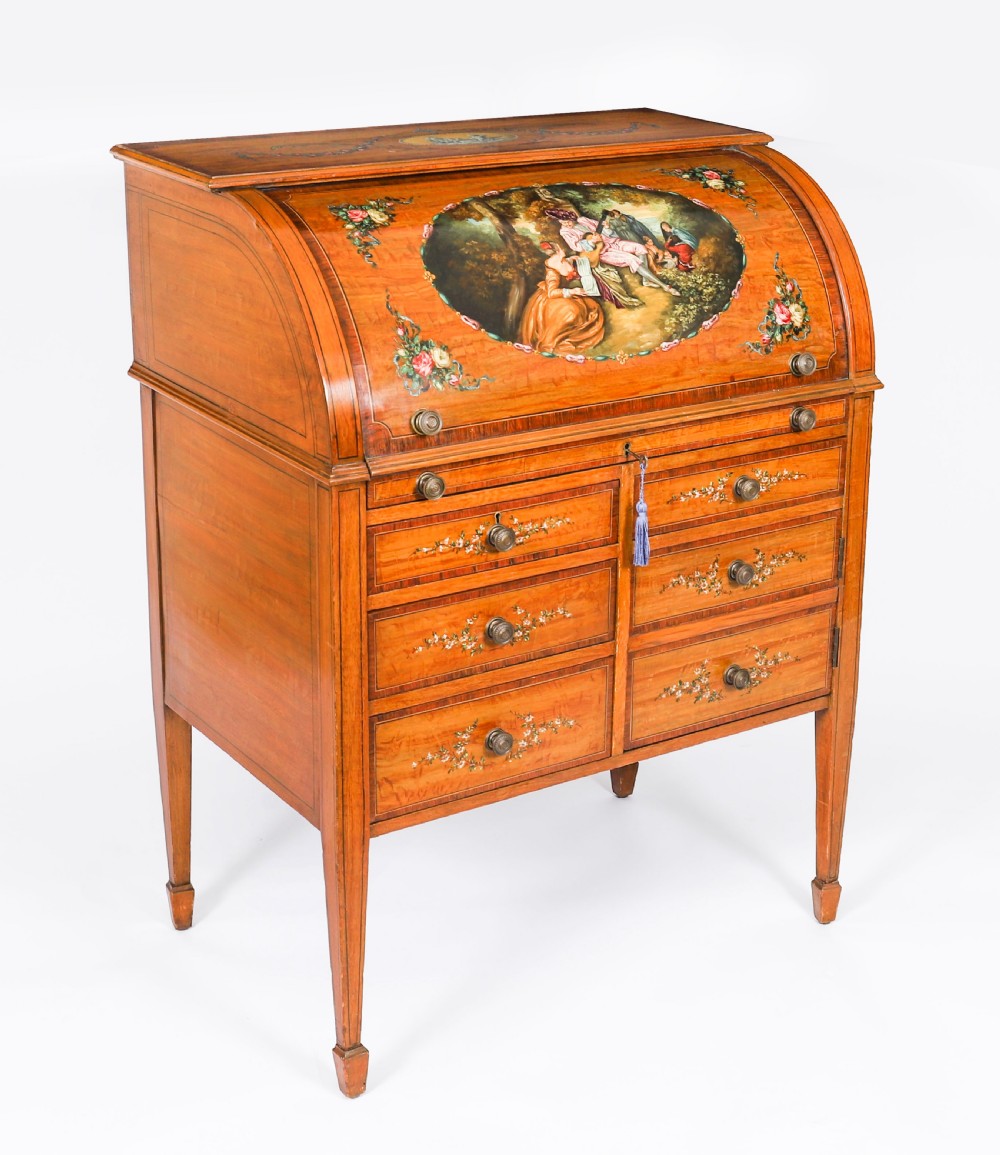 A late Victorian Sheraton Revival satinwood cylinder bureau featuring hand-painted floral swags, a central figural scene, and multiple small drawers above tapered legs.