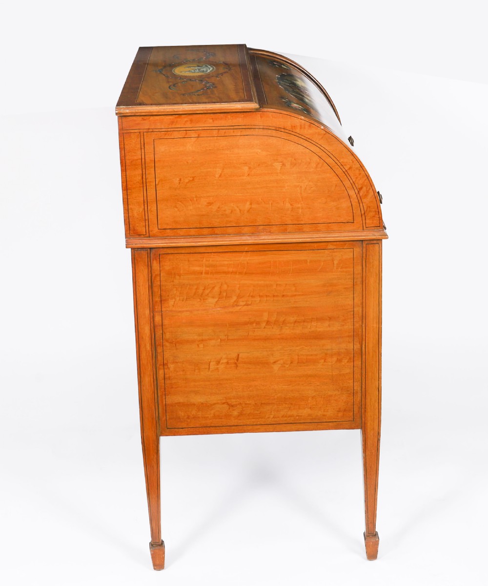 A late Victorian Sheraton Revival satinwood cylinder bureau featuring hand-painted floral swags, a central figural scene, and multiple small drawers above tapered legs. View IV