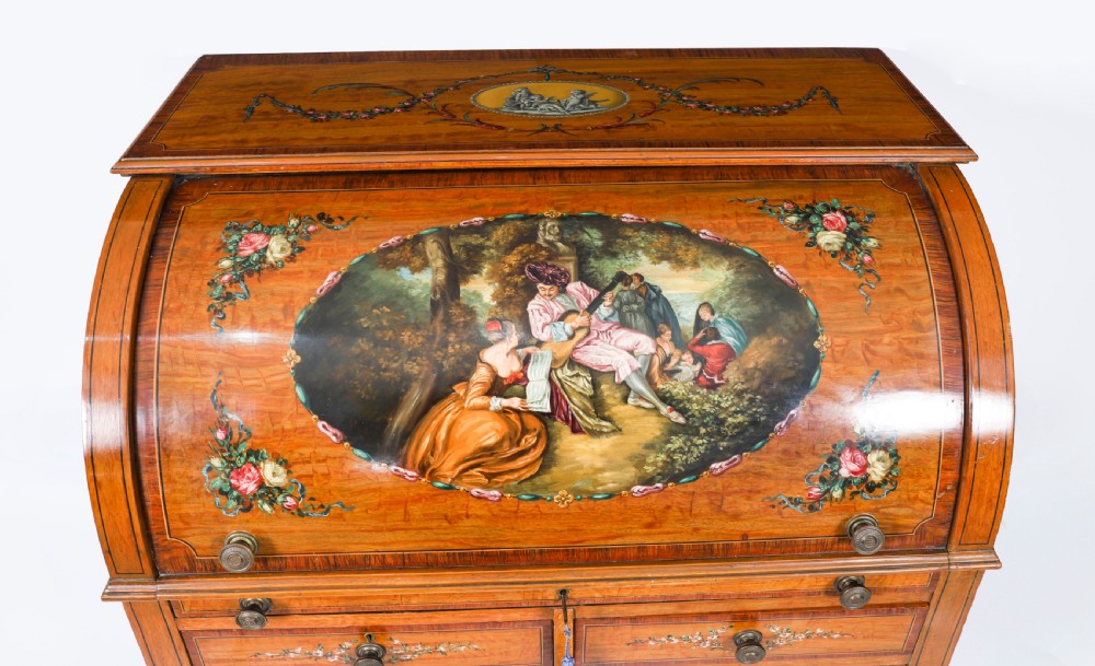 A late Victorian Sheraton Revival satinwood cylinder bureau featuring hand-painted floral swags, a central figural scene, and multiple small drawers above tapered legs. View V