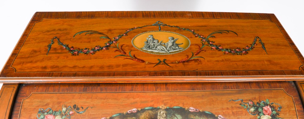 A late Victorian Sheraton Revival satinwood cylinder bureau featuring hand-painted floral swags, a central figural scene, and multiple small drawers above tapered legs. View IX