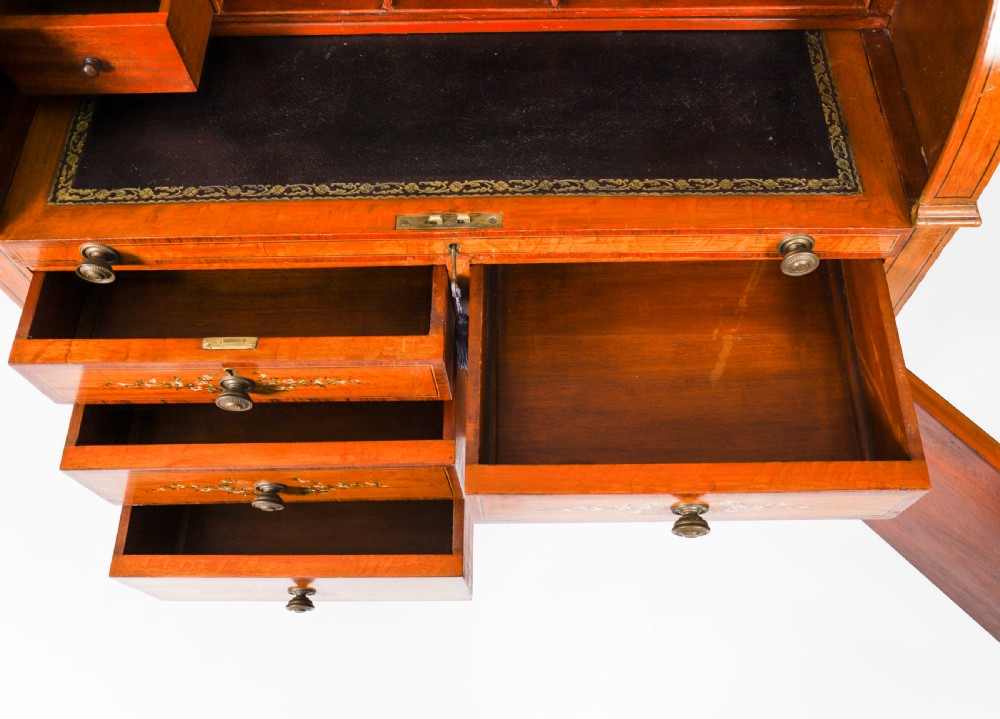 A late Victorian Sheraton Revival satinwood cylinder bureau featuring hand-painted floral swags, a central figural scene, and multiple small drawers above tapered legs. View XVI