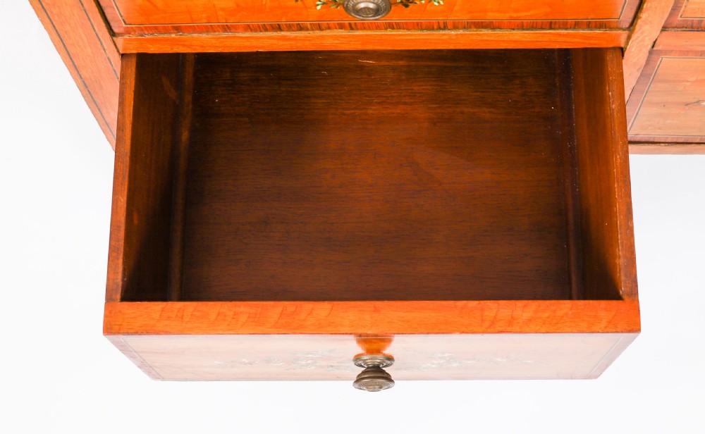 A late Victorian Sheraton Revival satinwood cylinder bureau featuring hand-painted floral swags, a central figural scene, and multiple small drawers above tapered legs. View XIX