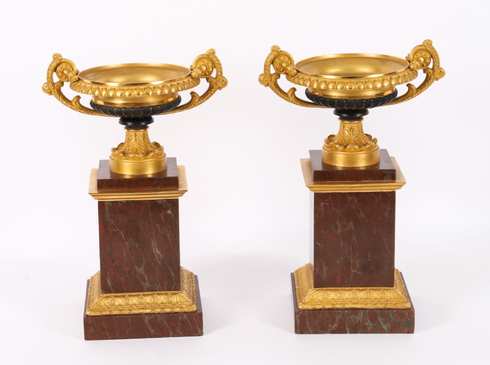 A pair of nineteenth-century French ormolu and bronze tazzas with scroll handles, mounted on tall rectangular red marble plinths.