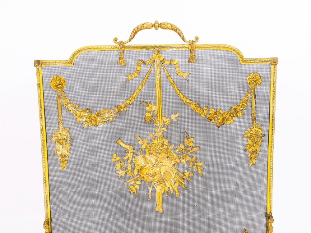 A 19th-century French gilt bronze fire screen featuring a woven mesh panel decorated with central musical trophy motifs, floral garlands, and ribbon swags. View II