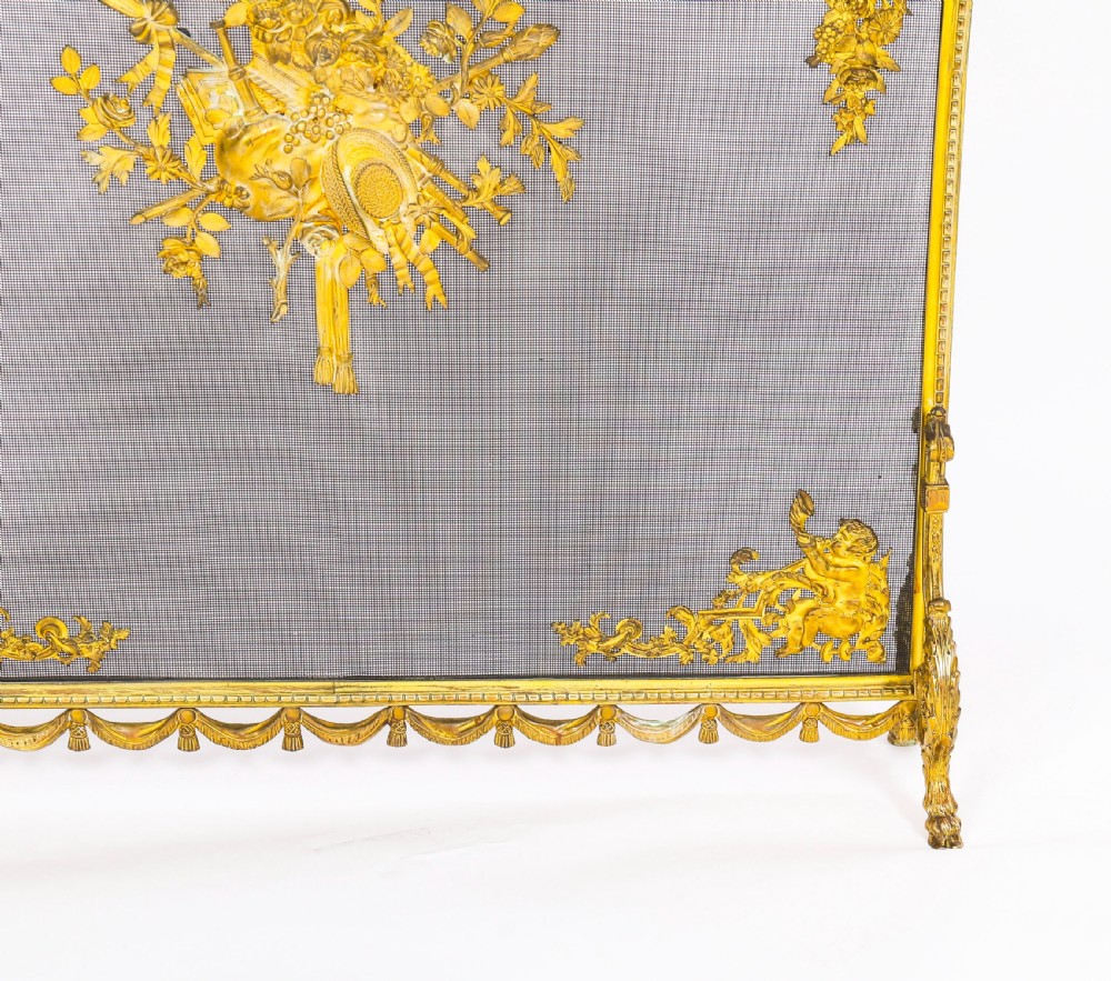 A 19th-century French gilt bronze fire screen featuring a woven mesh panel decorated with central musical trophy motifs, floral garlands, and ribbon swags. View VI