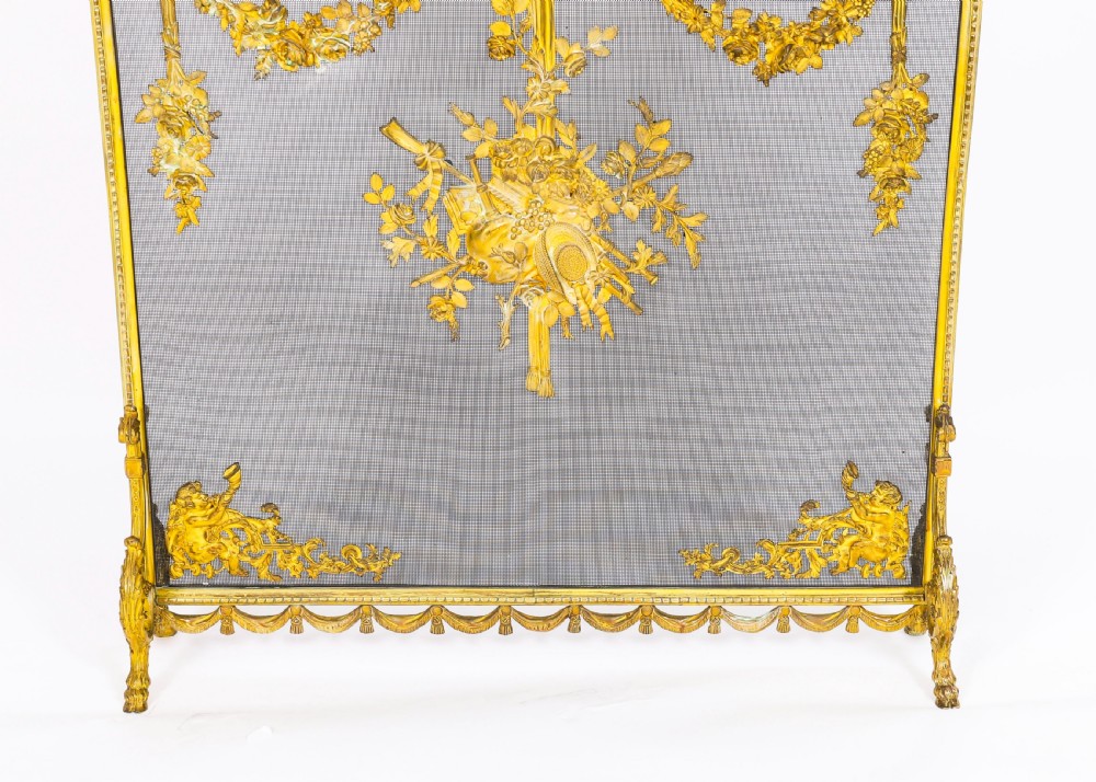 A 19th-century French gilt bronze fire screen featuring a woven mesh panel decorated with central musical trophy motifs, floral garlands, and ribbon swags. View VII